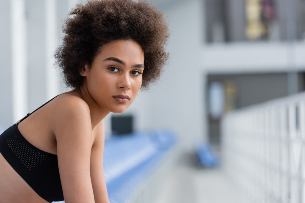 Young african american sportswoman in black top looking at camera on blurred stadium